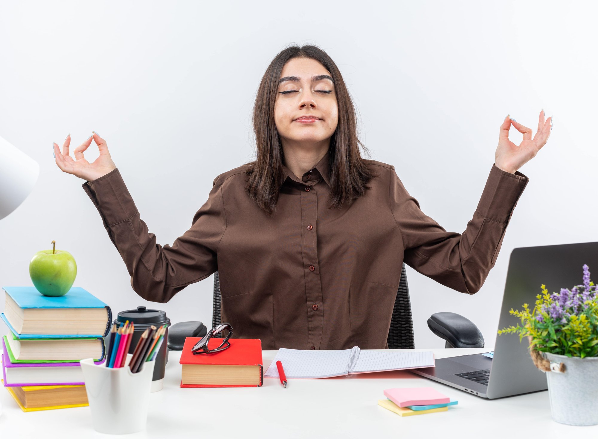 pleased-with-closed-eyes-young-school-woman-sits-table-with-school-tools-doing-meditation-gesture-min